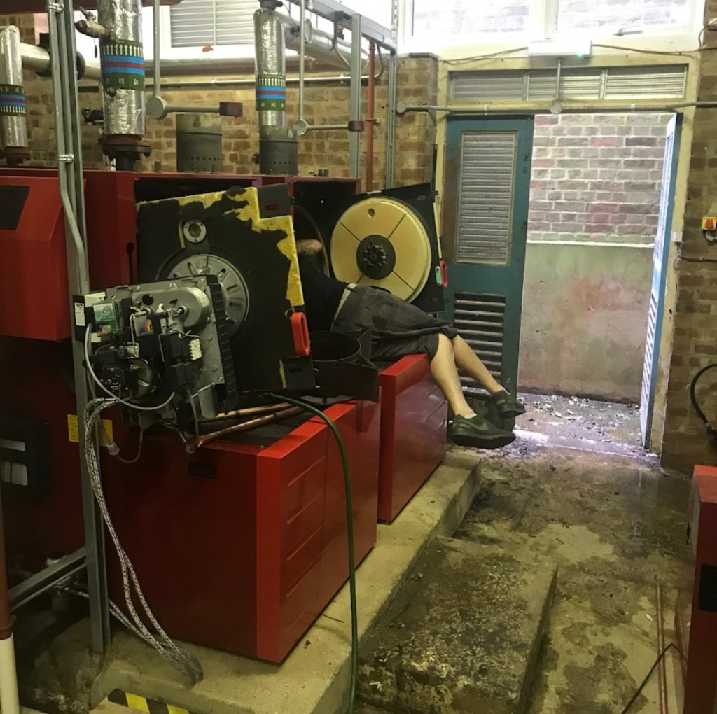 APS engineer servicing a red floor-standing commercial boiler in a brick plant room